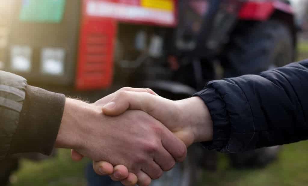 Agricultores dando as mãos com trator ao fundo