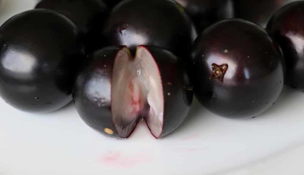 Frutas Jabuticabas com uma cortada ao meio mostrando a polpa