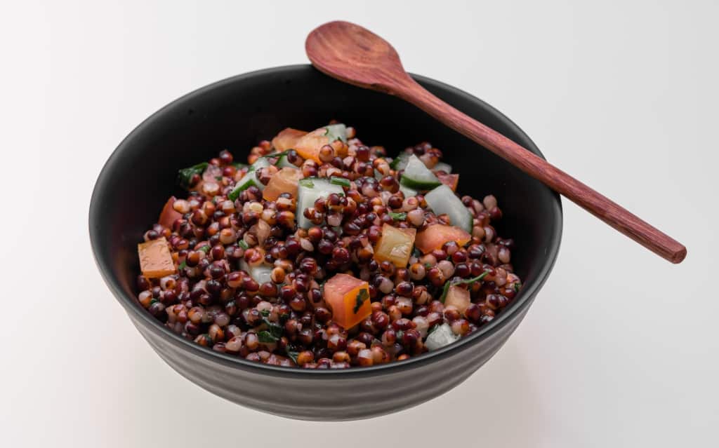 Tigela com sorgo, tomate e pepino e colher em cima