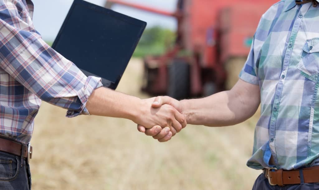 produtores dando as mãos com máquinas agrícolas ao fundo