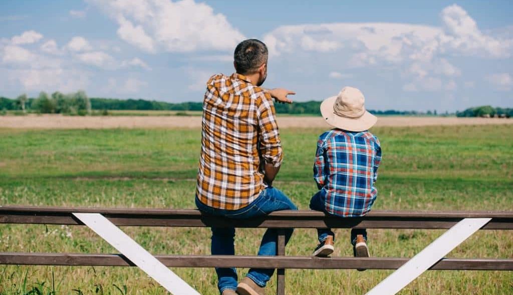 pai e filho sentados de costas na cerca observando a fazenda