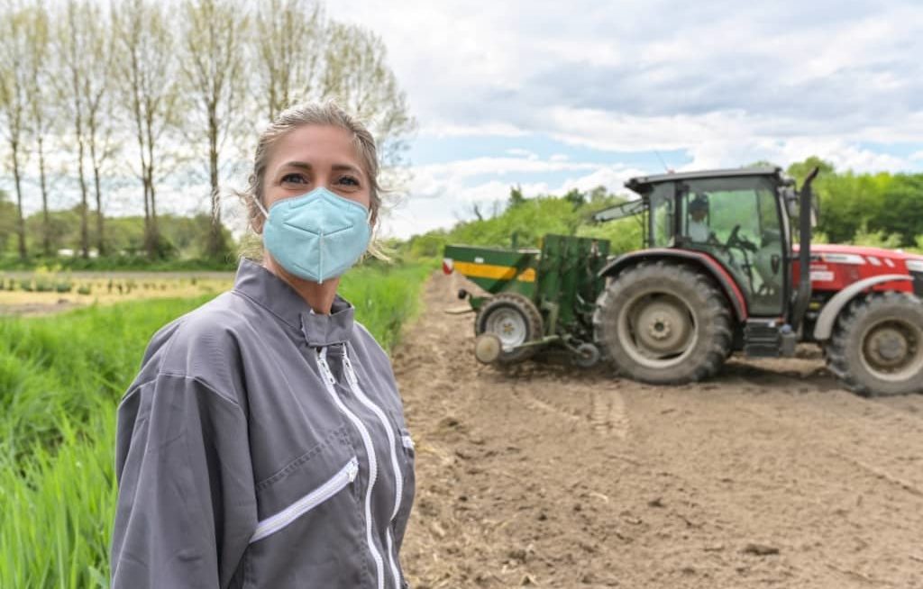 Agricultora com máscara na fazenda, trator ao fundo
