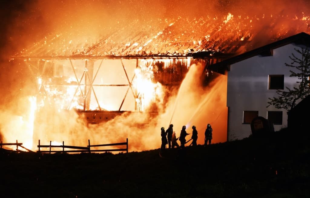 Incêndio em galpão de fazenda e bombeiros apagando o fogo