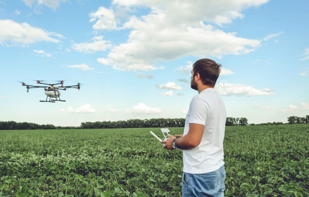 Homem pilotando drone pulverizador em cima de lavoura