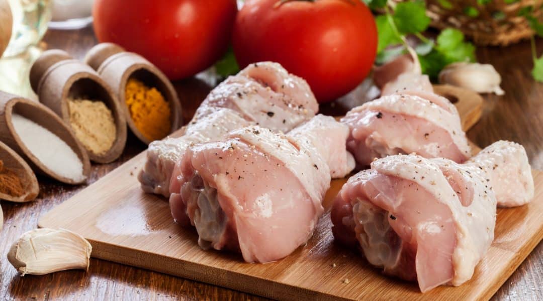 Pedaços de frango, ingredientes e temperos ao fundo