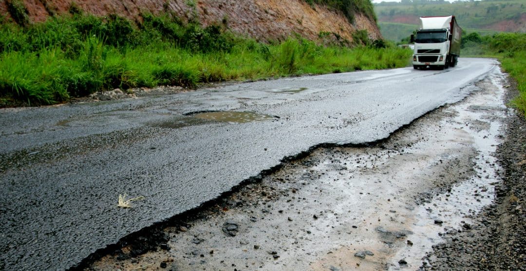Buracos em rodovia com carreta ao fundo