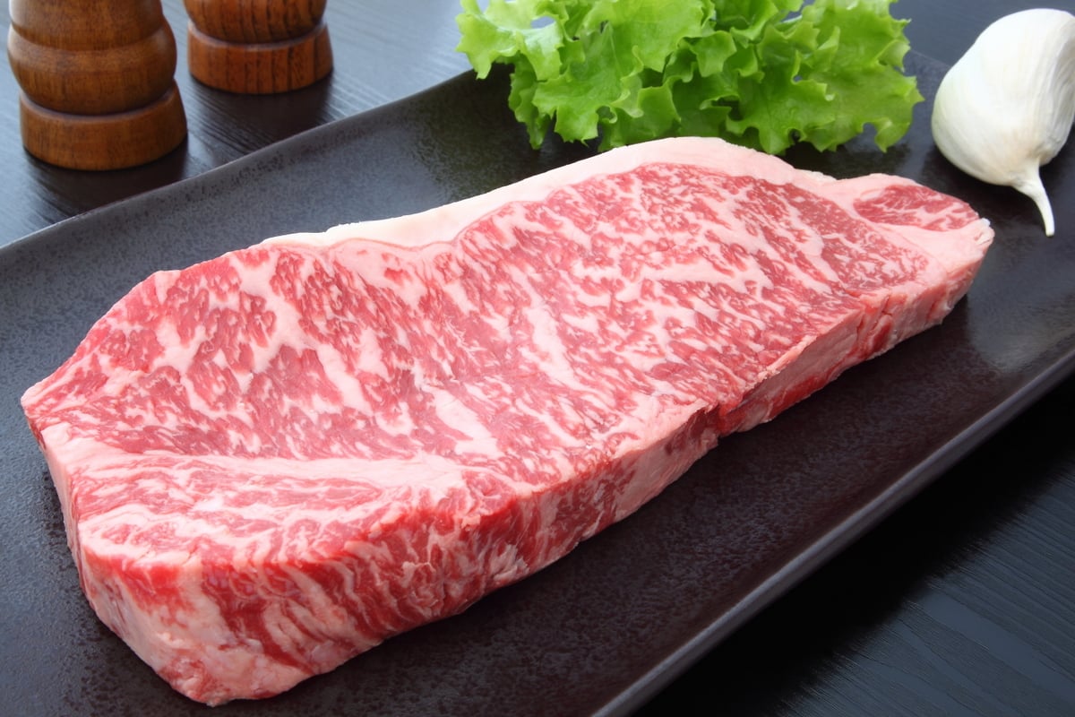 Bife de Wagyu em bandeja, acompanhado de alface, dente de alho e temperos ao fundo.