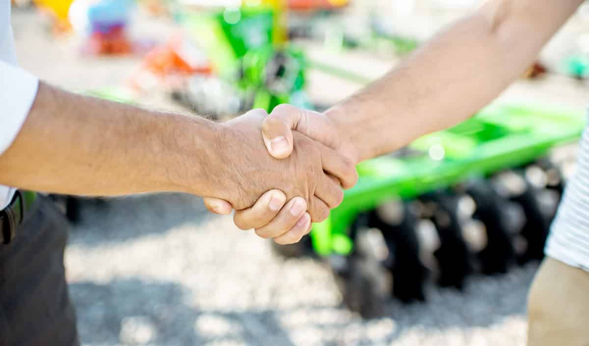 Homens se cumprimentam com máquina agrícola ao fundo