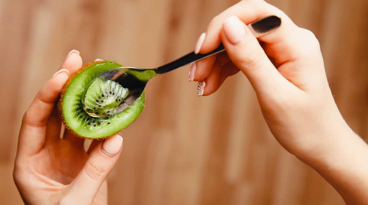 Mulher comendo kiwi com colher, benefícios.