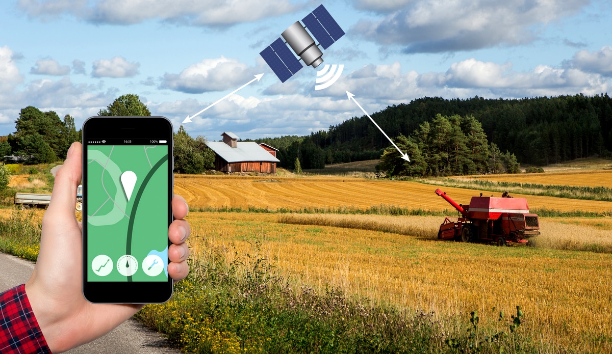 Homem segurando celular com conectividade em satélite, monitorando colhedora em campo