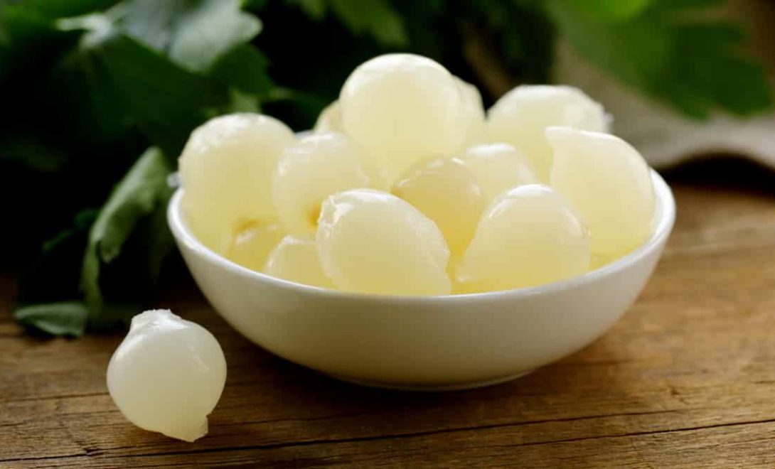 Cebolas do tipo pérola em um pote branco e temperos ao fundo