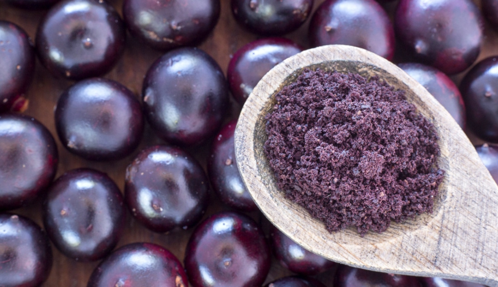 Frutos de açaí inteiros recobrindo a mesa e colher, logo acima, com a polpa da fruta amassada.