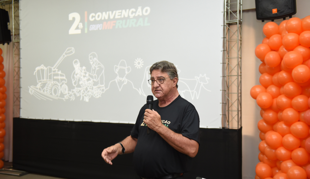Presidente do Grupo MF Rural, Wilson Lucas, faz a abertura do evento. Ao fundo, bexigas de cor laranja e telão com o nome do evento.