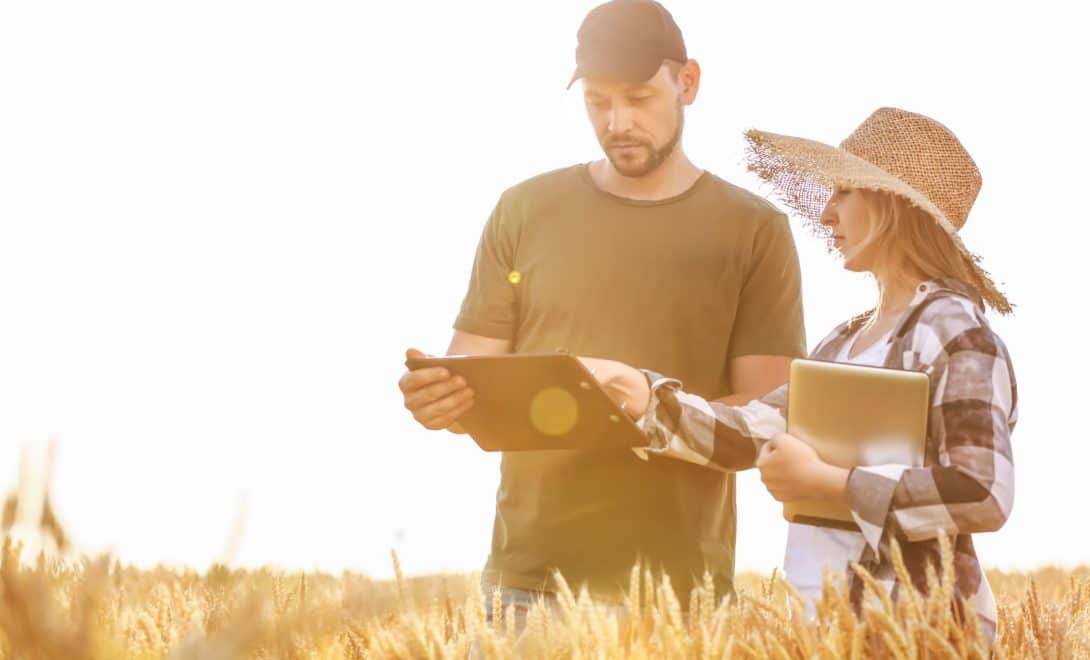 Homem e mulher em meio a plantação manuseando tablets para a análise de dados.