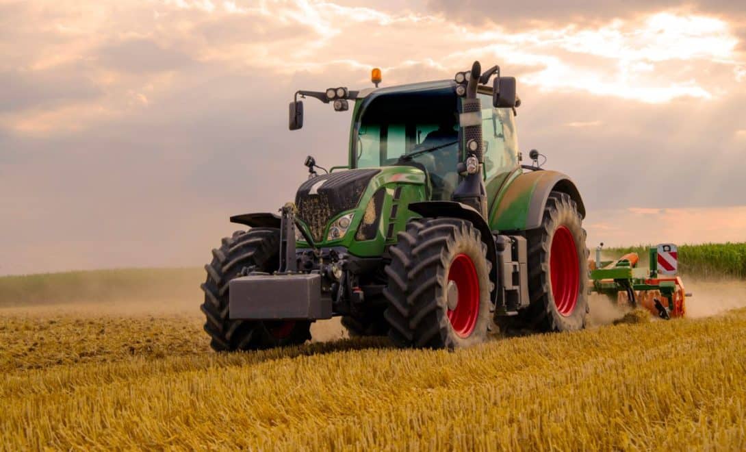 Trator de cor verde com implemento em plantação.