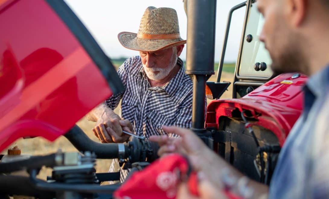 Dois homens analisando o motor de um trator