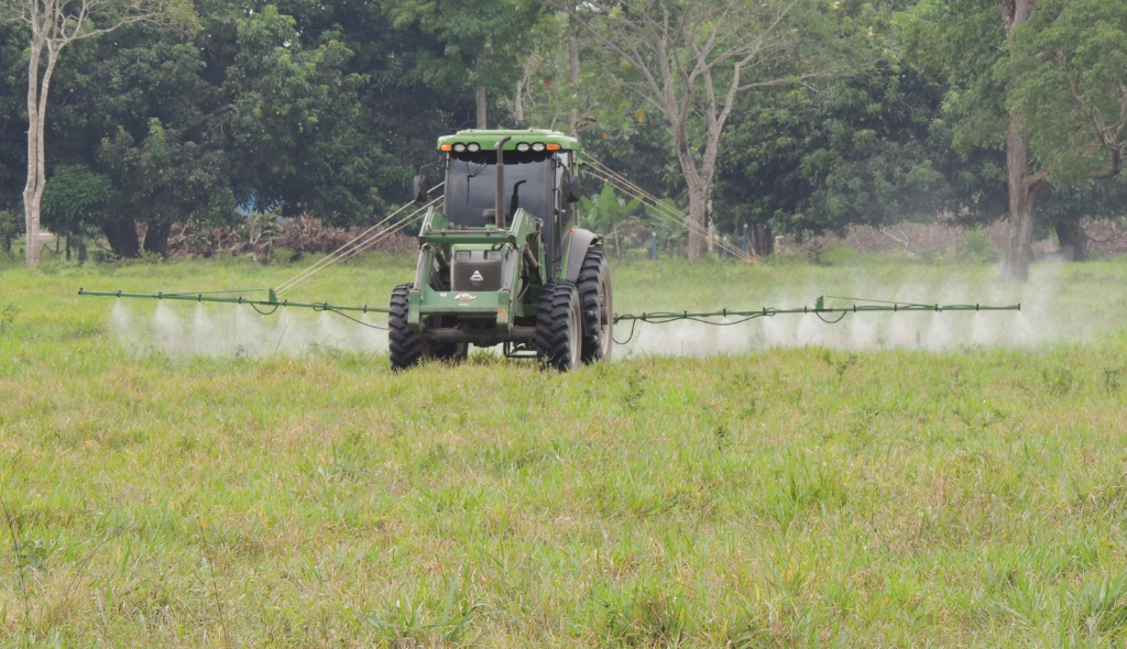 Trator na coloração verde realizando o controle químico de pastagem