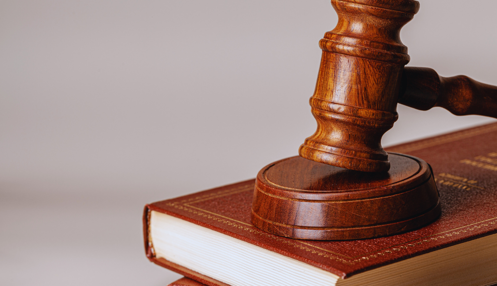 Martelo de juiz sobre livro de capa vermelha simboliza a justiça e a legislação vigente no Brasil.