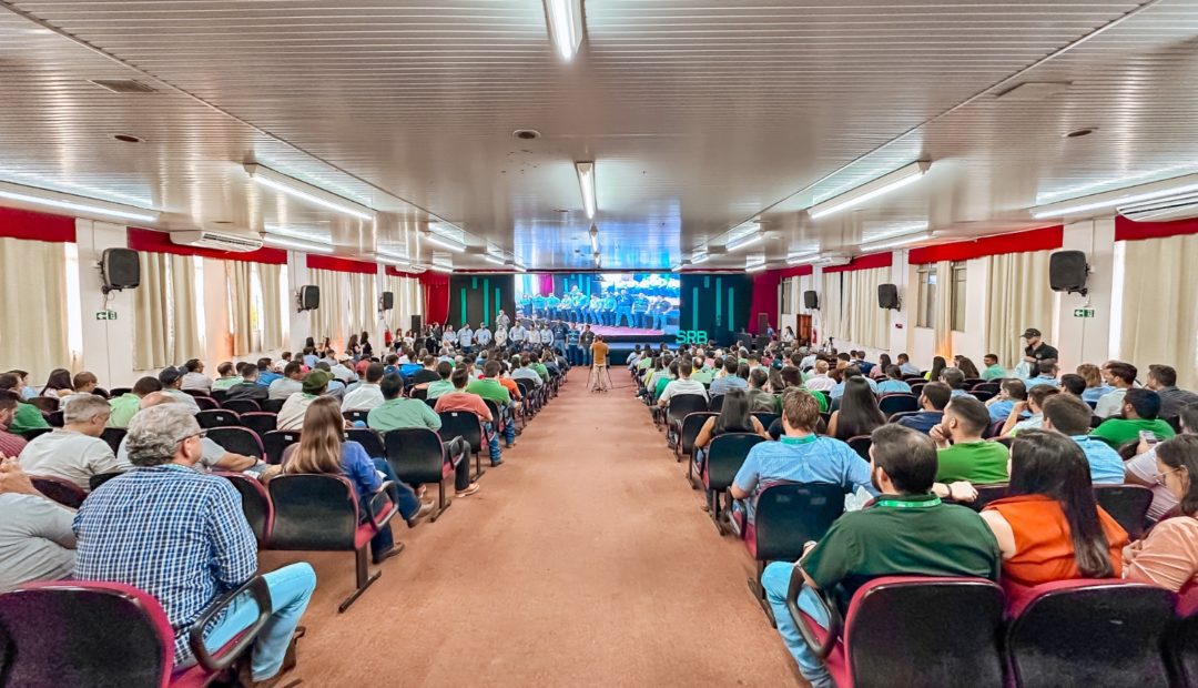Auditório lotado durante simpósio de reprodução bovina, com participantes atentos às palestras. No palco, especialistas e organizadores estão posicionados diante de um telão iluminado, reforçando o caráter técnico e científico do evento.