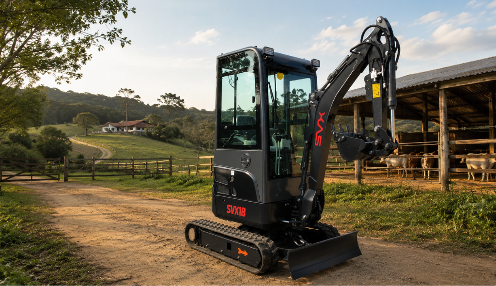 Mini Escavadeira SVX 18SKC Mini escavadeira SVX18 com cabine fechada estacionada em uma fazenda, ao lado de um curral com gado. A máquina está sobre uma estrada de terra, com o braço hidráulico recolhido e a lâmina frontal apoiada no solo. Ao fundo, há uma sede rural cercada por áreas verdes, cercas e colinas. A imagem destaca a versatilidade da mini escavadeira para atividades como abertura de valas, manutenção de estradas, limpeza de currais e serviços de infraestrutura em propriedades rurais.