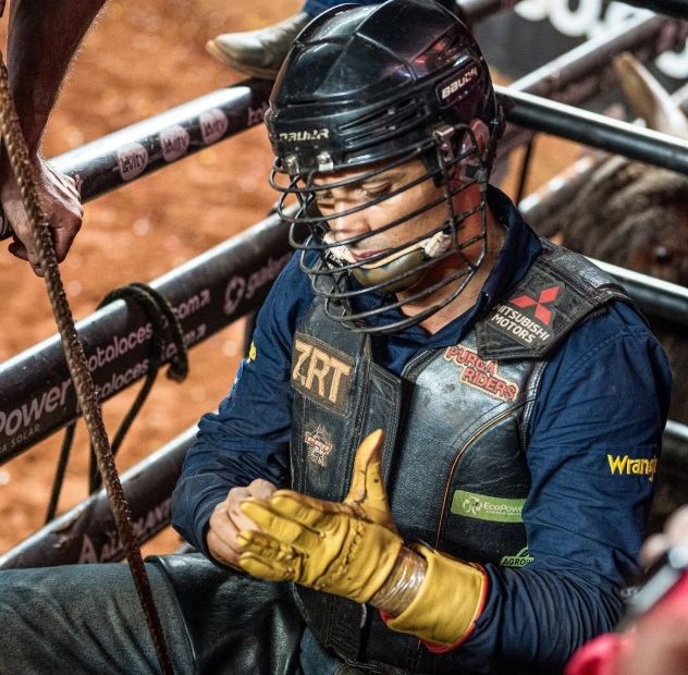 Peão de rodeio usando capacete, colete e luvas de proteção enquanto se prepara para a montaria em touros.